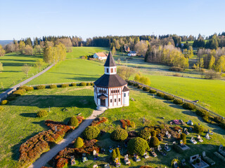 Set against a lush green landscape, Tesarov Chapel features a distinctive octagonal design. Its striking white exterior stands out in the serene surroundings of Korenov, Czechia, during a clear day.