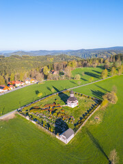 Tesarov Chapel stands majestically in Korenov, surrounded by a serene graveyard and lush green fields. The aerial perspective highlights the natural beauty of the Jizera Mountains.