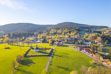 This aerial view captures Tesarov Chapel surrounded by a small graveyard in Korenov, located in the picturesque Jizera Mountains of Czechia. The landscape is lush and inviting during spring.
