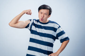 Asian man in striped shirt showing off his biceps with a proud facial expression, lips pursed in a...
