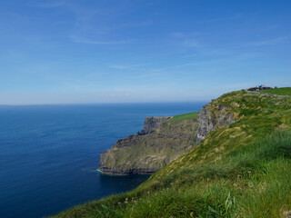 Fototapeta premium Steep cliffs rise dramatically above the deep blue ocean under a clear sky