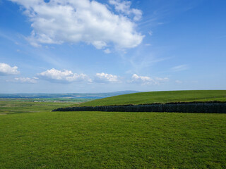 A stone wall cuts across rolling green fields under a sky dotted with fluffy white clouds