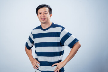 Asian man in navy and white striped t-shirt smiling confidently with hands on hips, standing in relaxed posture against plain light background, perfect for profile, branding, or editorial use