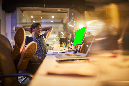Young man relaxing at his desk with feet up and arms behind head in a modern office