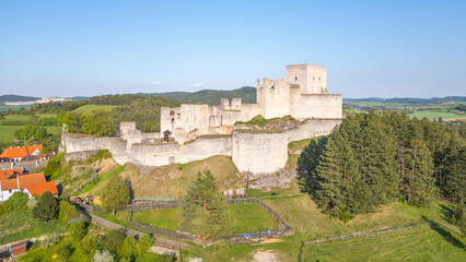 Rabi Castle ruins stand majestically against the backdrop of Czech countryside. This drone view showcases the historical structure surrounded by lush greenery and distant hills on a clear day.