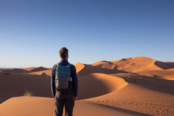 outdoor adventure travel in Sahara desert sand dunes, man with backpack standing alone