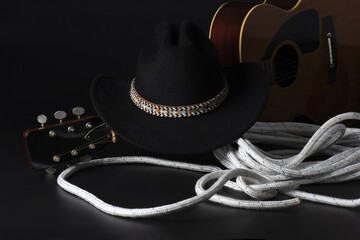 Cappello da cowboy, chitarra e corda su sfondo nero. 