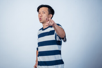 Asian man in striped shirt pointing directly at the camera with a serious expression, standing...