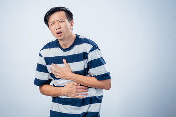 Asian man in striped shirt showing pain and discomfort while holding his chest and stomach,...