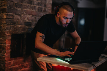 Man using a laptop and headphones to produce music in a stylish indoor setting. The environment is...