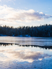 Reflective frozen lake in winter with snowy trees, clouds and skies in sweden