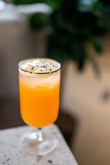 A vibrant orange cocktail served in a tall glass with frothy white foam, garnished with black sesame seeds. Placed on marble surface with a blurred background, highlighting its refreshing presentation