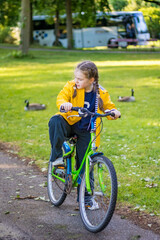 Young girl in yellow raincoat with bag and flowers riding a bicycle in Deventer city. High quality photo