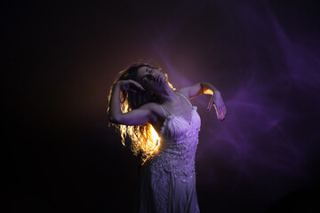 Serene dancer in white dress moving gracefully through beams of atmospheric backlight.