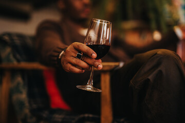 A person rests in a cozy ambiance while holding a glass of red wine, symbolizing relaxation and sophistication. Captured indoors with warm lighting, the image inspires calmness and enjoyment.