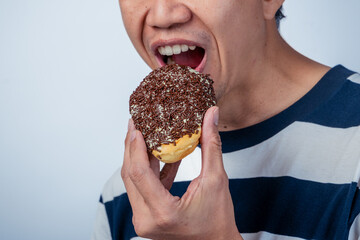 Close-up of an Asian man about to eat a donut covered with chocolate sprinkles, holding it near his...