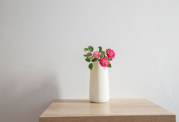 pink roses in ceramic vase on wooden table  in white interior