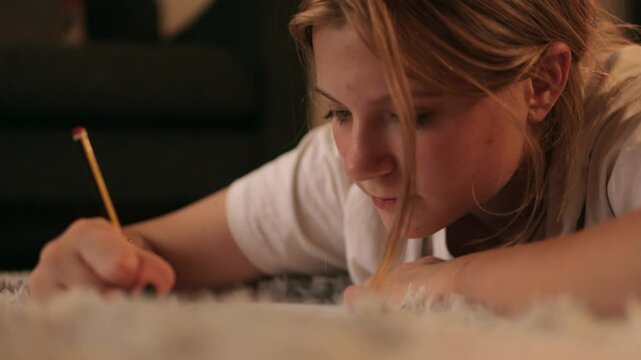 Teenager girl  student writing study notes while reclining on bed, intensely focused on academic preparation in cozy home learning space.Lifestyle concept .Education online.