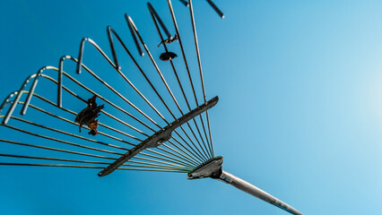 Metal leaf rake on blue sky background at sunny day. Metal rake tines silhouetted on sky...