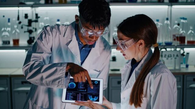 Scientific Collaboration in Laboratory: A pair of dedicated researchers, immersed in their crucial scientific work, are intensely focused on a tablet device within a state-of-the-art laboratory.