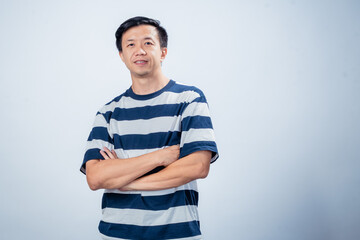 Asian man in navy and white striped t-shirt crossing arms while looking confidently at the camera, posing against plain light background, conveying attitude, confidence, and modern style