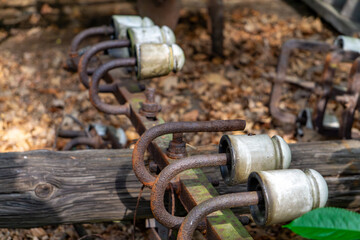 old rusty porcelain insulators mounted on a wooden part of an electric pole, lying among dry leaves. A remnant of an abandoned power line installation