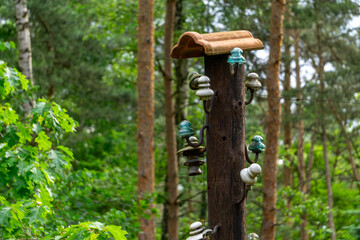 Old wooden utility pole with ceramic insulators, partially covered with a roof tile, standing among trees in a forest. A remnant of former electrical infrastructure in a natural setting.