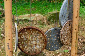 Rusty perforated metal lids hanging on wires between posts, serving as improvised garden chimes....