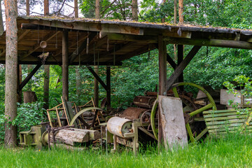 roofed wooden shelter in the forest with abandoned old agricultural machines and wooden parts. The...
