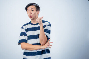 Asian man in striped shirt smiling confidently while showing a thumbs-up gesture with one hand, standing against a plain light background with a friendly and positive expression