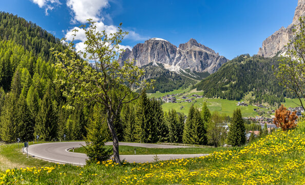 Lush green meadows, a curvy road and the Dolomites mountain range in Northern Italy