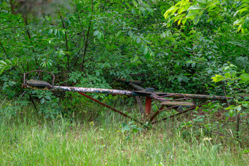 rusty, abandoned children's carousel surrounded by tall grass and dense bushes. Faded paint and...