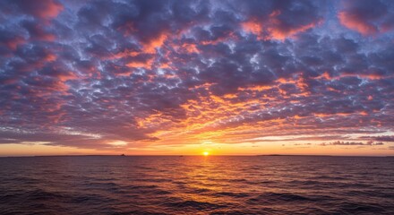 Obraz premium Colorful sunset over calm ocean; clouds scattered, golden horizon light reflecting in water