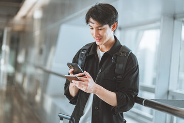 Happy traveling asian man uses mobile smartphone hold passport, checking trip destination on...