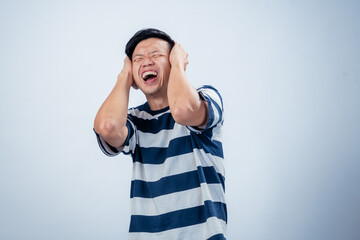 Asian man in striped shirt covering his ears with both hands and yelling in frustration, expressing...