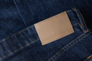 Empty leather tag or label on blue denim jeans clothes top view. Shopping, sale and fabric industry background.