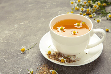 Aromatic herbal tea in white cup and chamomiles on grey concrete background. Space for text