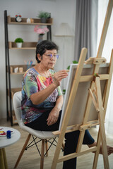 Senior woman focuses on her painting at home, enjoying creativity and relaxation, expressing...