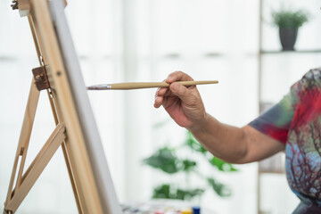 Artist creating masterpiece with paintbrush at easel in bright studio filled with plants, natural...