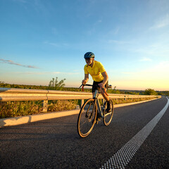Naklejka premium Cyclist leans forward during acceleration phase of intense training ride, surrounded by sunset glow and smooth country road. Concept of sport, race preparation, cycling, endurance, speed