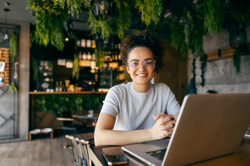 Portrait of multicultural female freelancer sitting in cafe with laptop in front of her.