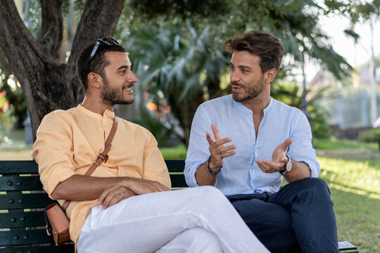 Two young men, friends or colleagues, having a positive conversation on a park bench outdoors. - Powered by Adobe