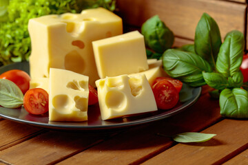 Swiss cheese, green basil, salad, and tomatoes on a wooden table.