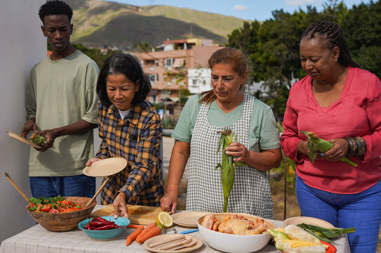 Group of multiracial friends having fun preparing food for barbecue dinner at house rooftop - Summer party, diverse people and bbq dinner concept - Powered by Adobe