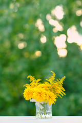 beautiful floral composition with yellow flowers in glass vase on table in garden, natural background. rudbeckia laciniata (rudbeckia golden ball), symbol of summer or autumn season.