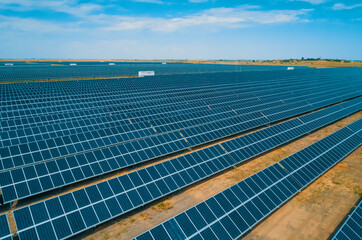 Expansive solar panel arrays under a clear blue sky in a vast renewable energy farm