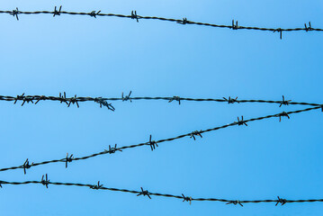 Barbed wire against a clear blue sky creates a stark silhouette at midday in an open area