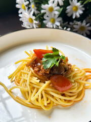A serving of spaghetti adorned with a rich tomato-based sauce, garnished with fresh herbs. Presented on a white plate, it showcases the delicious combination of Italian-inspired flavors and textures.