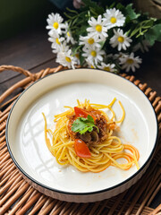 A serving of spaghetti adorned with a rich tomato-based sauce, garnished with fresh herbs. Presented on a white plate, it showcases the delicious combination of Italian-inspired flavors and textures.