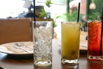  Iced drinks in tall glasses with straws on a restaurant table, featuring iced, citrus juice, and...